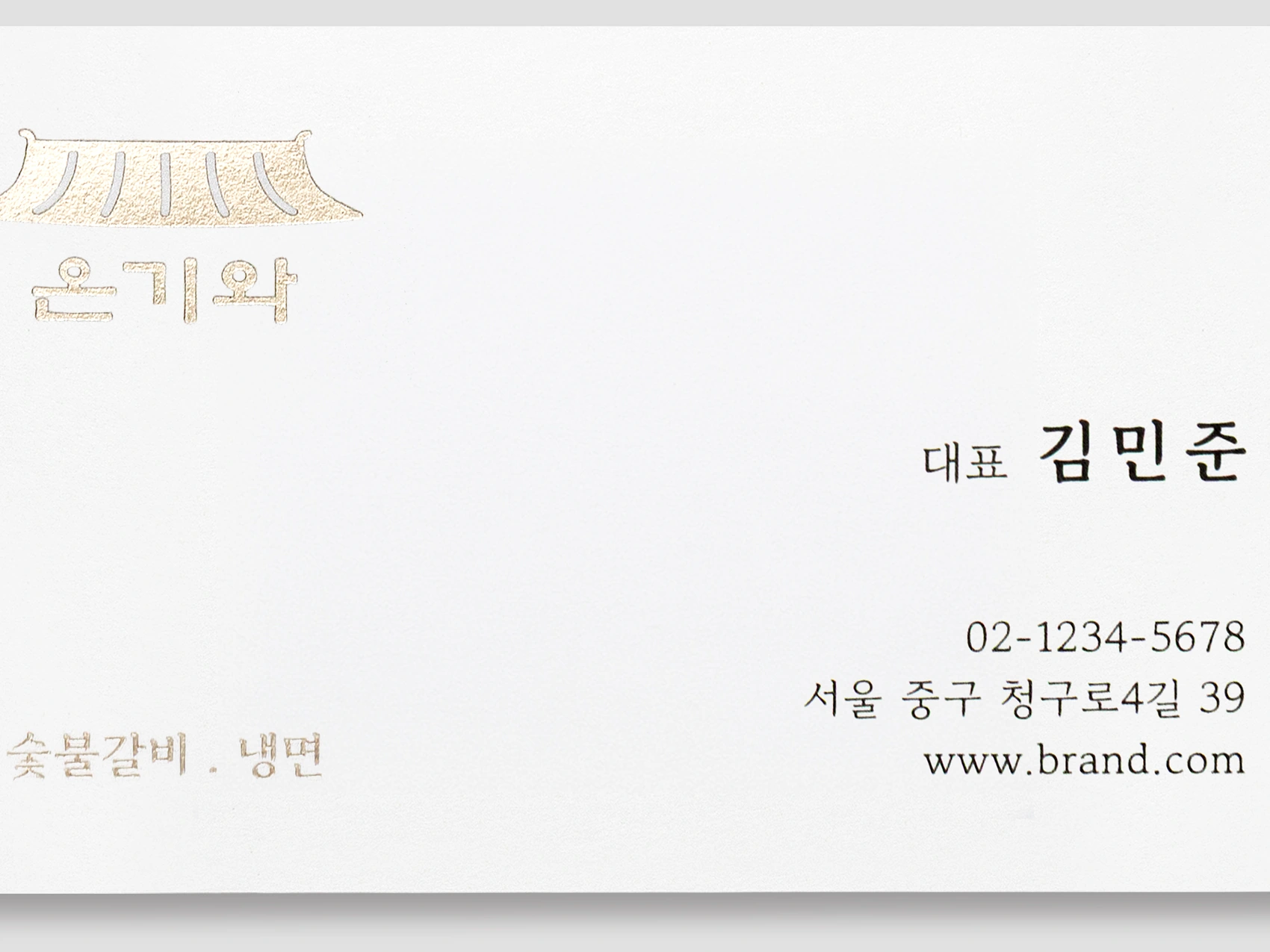 흰색 가로형 명함의 작은 금박 로고와 이름 접사